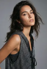 Chaleco de punto calado color beige, sin mangas, con capucha y bolsillos delanteros.