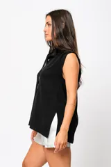 Camisa negra sin mangas con cuello mao adornado con un delicado volado y cierre frontal con botones.