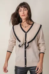 Cárdigan negro de punto fino con hilos de lurex, cuello en V calado con volados color crema, cierre frontal con botones con strass y puños anchos con ribete color crema.