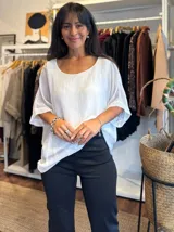 Blusa de seda blanca con corte holgado, cuello redondo y mangas cortas con caída suave. Presenta un diseño minimalista con espalda ajustable mediante lazo.