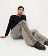 Pantalón jean de corte super baggy con piernas amplias, confeccionado en denim de algodón. Presenta un acabado lavado grisáceo, ruedo desflecado y detalle de costura frontal tipo nesga.