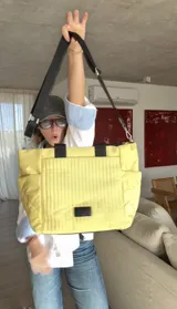 Cartera tipo tote de nylon color malva, con diseño capitoneado de líneas verticales en el frente y rombos en los laterales. Cuenta con doble asa de mano en color negro, bolsillos laterales y un parche decorativo con logo en la parte frontal.