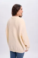 Buzo de punto color crudo, con cuello redondo y mangas largas, de diseño holgado y acabado clásico.
