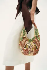 Bolso de hombro con diseño estructurado, decorado con intrincados bordados de abalorios, cuentas y apliques en tonos tierra, verde y crema. Presenta un asa integrada y cierre mediante botón imantado.