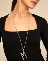 Dije con forma de letra M, bañado en oro, con diseño inspirado en un clavo. Pieza artesanal de estilo minimalista.