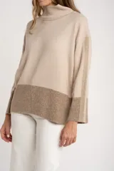 Sweater tipo polera de calce oversize, con diseño color block que combina tonos beige y marrón. Presenta cuello alto, mangas largas con puños acanalados y un panel inferior acanalado a juego.
