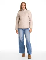 Campera 3 en 1 de color beige, con sistema de capas desmontables. La capa exterior es de tejido técnico resistente al viento y lluvia ligera, con capucha fija, cierre frontal con solapa, bolsillos de parche y ajuste elástico interno en la cintura. Incluye una campera interior capitoneada ultraliviana que puede usarse de forma independiente.