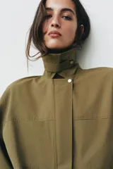 Vestido corto verde militar de cuello solapa y manga larga, con bolsillos de plastrón en el delantero y cierre frontal con cremallera oculta por sopata. Cuenta con un cinturón incorporado del mismo tejido con hebilla metálica y aberturas laterales en el bajo.