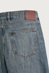 Jeans flare fit de denim rígido en color azul con efecto lavado. Presentan tiro medio, diseño de cinco bolsillos y cierre frontal con cremallera y botón.