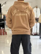 Canguro oversize beige con capucha y cordones ajustables, bolsillo tipo canguro y pequeño bordado en el pecho.
