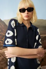 Vestido corto de punto jacquard color azul marino, con diseño de estrellas blancas alineadas verticalmente en los laterales. Presenta cuello polo con cierre frontal de botones y mangas cortas con detalles de rayas en contraste.