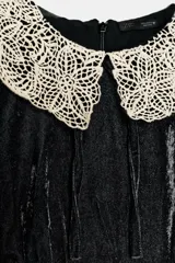 Camisa de terciopelo negro con cuello solapa grande en crochet color crema y detalles de crochet en los bordes de las mangas cortas. Presenta un diseño entallado con cierre de cremallera en la espalda.