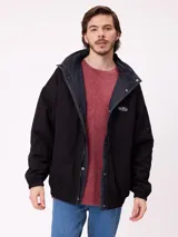 Campera reversible con capucha oculta, confeccionada en sarga de algodón con elastano en el exterior y nylon de poliéster en el interior. Presenta cierre frontal con botones a presión, costuras visibles en contraste y puños elásticos.