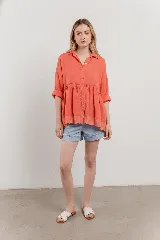 Blusa de lino color coral con corte evasé, caída fluida, mangas relajadas y botones frontales. Presenta un detalle de bordado calado en el dobladillo.
