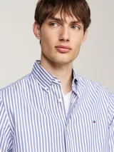 Camisa de hombre Tommy Hilfiger de corte slim, confeccionada en popelín de algodón con tecnología Flex. Diseño a rayas verticales azules y blancas, cuello con botones y logo bordado en el pecho.