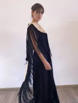 Poncho estructurado color beige con diseño asimétrico, más corto en el frente y largo en la parte posterior. Presenta un bordado de ardilla con lentejuelas en la espalda y flecos largos negros que rodean toda la prenda.