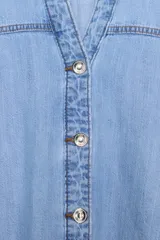 Camisa de denim en tono azul claro, con cuello solapa, escote en pico y cierre frontal con botones. Presenta mangas anchas por debajo del codo y un diseño de bajo asimétrico.