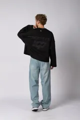 Buzo de cuello redondo confeccionado en tejido rústico con bordes al corte y costuras expuestas. Presenta un diseño boxy con estampado frontal y es reversible, permitiendo su uso por ambos lados.