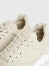 Zapatillas deportivas de mujer Calvin Klein, color beige claro, con cordones y suela gruesa blanca. Presentan una combinación de materiales que incluye piel natural y ecológica, con paneles de malla y detalles de monograma sutil en el lateral.