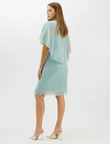 Vestido midi de tejido metalizado color turquesa, con sobrecapa de tul liviano sobre los hombros, detalle de pedrería en la cintura, volado lateral y tajo frontal.