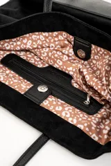 Bolso tipo tote de gran tamaño confeccionado en material sintético con acabado efecto gamuza en color tostado. Presenta doble asa larga en tono contrastante y placa metálica pequeña con logo de la marca en la parte frontal.