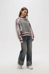 Campera de punto con cierre frontal, cuello alto y diseño de rayas laterales en mangas. Presenta un patrón texturizado en el cuerpo y detalles de rib acanalado en puños, cuello y ruedo.