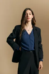 Camisa negra de manga larga con escote en V y cierre frontal de botones. Presenta detalles de volados en los hombros, frunces en la espalda y puños elastizados que le otorgan una silueta relajada y fluida.