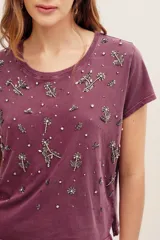 Remera de algodón color morado, con mangas cortas, cuello redondo y bordado de cuentas y pedrería en la parte frontal.