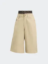 Bermuda color beige de corte ancho con tres líneas verticales a los costados y logo de la marca bordado en la pierna izquierda.