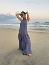 Vestido largo color gris azulado de crepe texturado, con cuello halter alto con volados, espalda descubierta y falda amplia con maxi volado inferior.