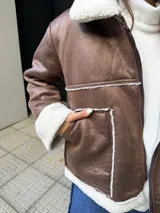 Campera tipo gamulán color marrón con interior y solapas de corderito sintético en color crema. Presenta cierre frontal, bolsillos laterales y diseño de corte holgado.