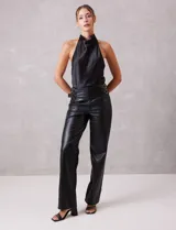 Pantalón de cuero sintético negro, de corte recto y tiro alto. Presenta cintura con hebillas laterales regulables y cierre frontal.