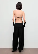 Top negro de cuello halter con diseño drapeado y bajo asimétrico. Presenta espalda abierta con tiras y cierre de botones en el cuello.