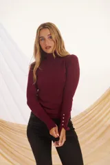 Polera de punto color borgoña, de cuello alto y manga larga con detalle de botones plateados en los puños.