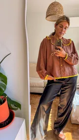 Camisa de color marrón chocolate con cuello redondo grande y ribetes en color amarillo vibrante. Presenta cierre frontal con botones amarillos, mangas largas con puños elásticos y un corte holgado.