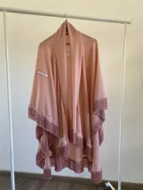 Ruana de tela fina color rosa, con diseño abierto y terminaciones con flecos largos en todo el borde inferior y laterales.