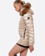 Campera puffer color beige con relleno de plumón, cierre central con cremallera de doble carro, bolsillos laterales y capucha desmontable con borde de piel sintética marrón. Largo 70cm.