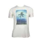 Remera blanca de manga corta con estampado fotográfico central de una palmera en un paisaje tropical.