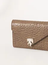 Billetera de cuero vacuno con textura graneada en color marrón. Presenta un diseño tipo sobre con cierre magnético y un aplique metálico distintivo en forma de llama en la parte frontal.
