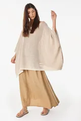 Blusa de punto estilo poncho en color beige, con diseño amplio, cuello redondo y aplique de etiqueta con el logo de la marca en el borde inferior.