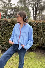 Camisa celeste a rayas con cuello y botonera decorados con bordado artesanal en hilo rojo, de corte clásico y mangas largas.