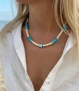 Collar corto de piedras reconstituidas blancas y escallas de turquesa, con un dije central en forma de estrella de nácar y cierre de acero.