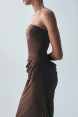 Vestido midi de escote recto sin tirantes, color marrón, con diseño semitransparente en la sección del abdomen y detalle drapeado en la falda. Cuenta con cierre lateral.