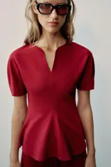 Top peplum confeccionado en hilatura de algodón de color bordó, con escote en V pronunciado, mangas cortas abullonadas y bajo con vuelo.