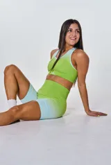 Conjunto deportivo de dos piezas compuesto por un top deportivo de cuello redondo y un short de tiro alto, ambos con diseño degradado en tonos verde lima y celeste. El top presenta el logo de la marca estampado en el frente.