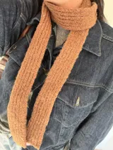 Bufanda angosta de tejido de punto color marrón, diseñada para anudar tipo corbatín. Confeccionada en poliéster.