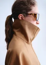 Chaqueta oversize color tostado con cuello embudo, manga larga, bolsillos laterales y bolsillos de parche con solapa. Cuenta con cierre delantero de cremallera y botones ocultos bajo tapeta, y forro interior.