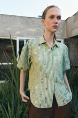 Camisa de corte recto en color verde claro con estampado de rayas verticales y detalles de lentejuelas brillantes. Presenta cuello solapa, cierre frontal con botones y mangas tres cuartos.