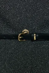 Chaleco jaspeado en tonos grises, con cuello redondo y sin mangas. Presenta cierre frontal con botones dorados y un cinturón fino negro con hebilla dorada.