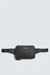 Riñonera negra con textura grabada, compartimento principal con cierre de cremallera y bolsillo frontal plano. Incluye asa ajustable con hebilla metálica de liberación rápida.